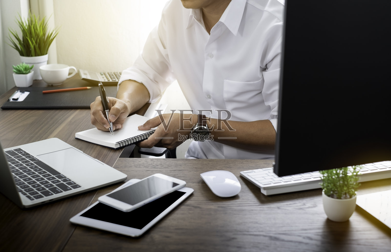 商人手持书写笔,将备忘录放入笔记本纸上,放在办公桌上办公。办公场所有电脑和笔记本电脑的拷贝空间。企业工作和学习的教育理念。照片摄影图片