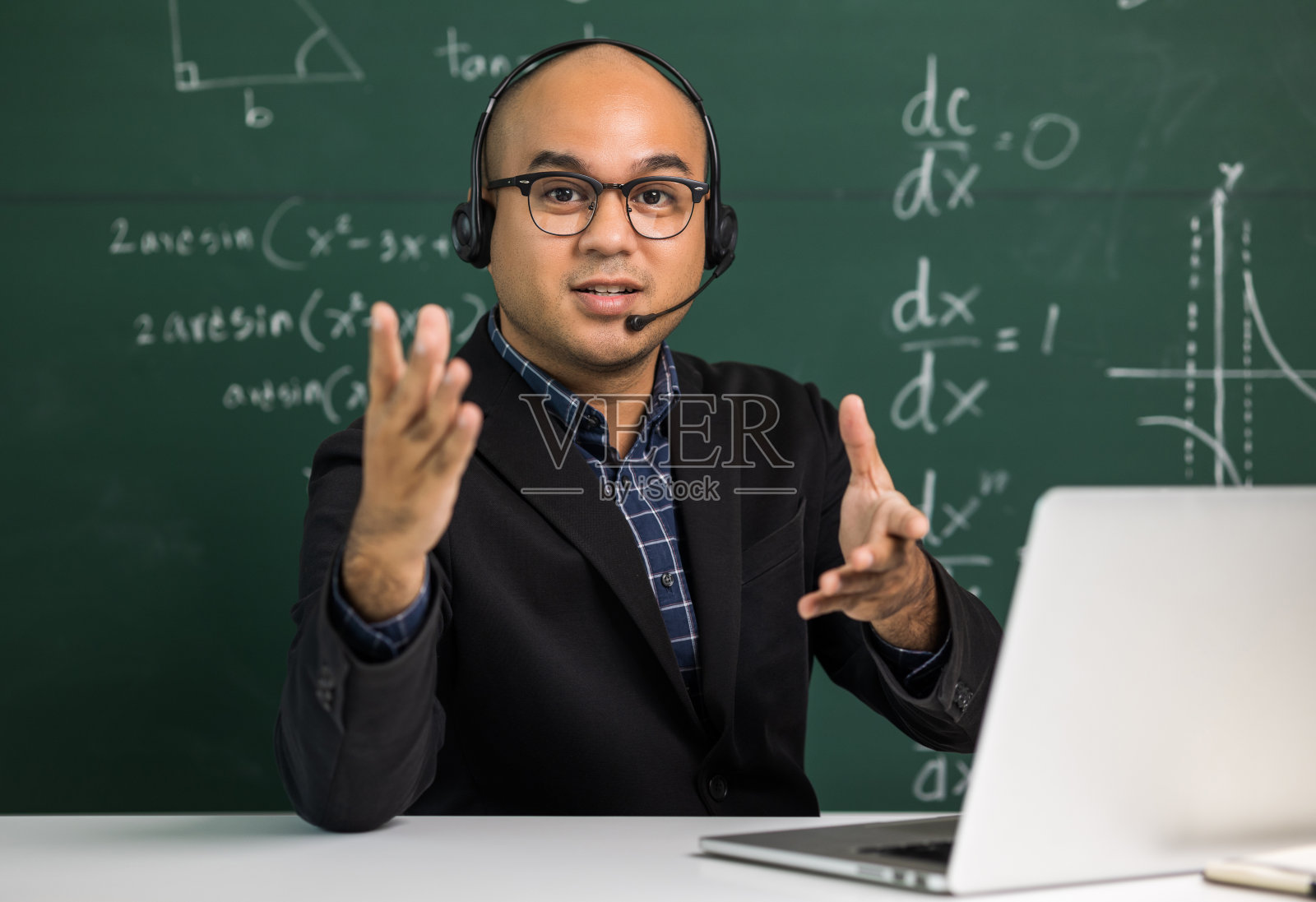 印度年轻教师男子看着摄像机坐在教学在线视频会议直播。亚洲教师戴着耳机课堂授课,为学生在线学习提供在线研讨会。照片摄影图片