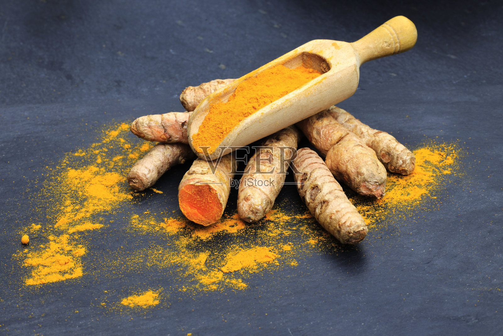 姜黄粉放在木勺里,根放在深色的桌子上(姜黄),Kurkuma照片摄影图片