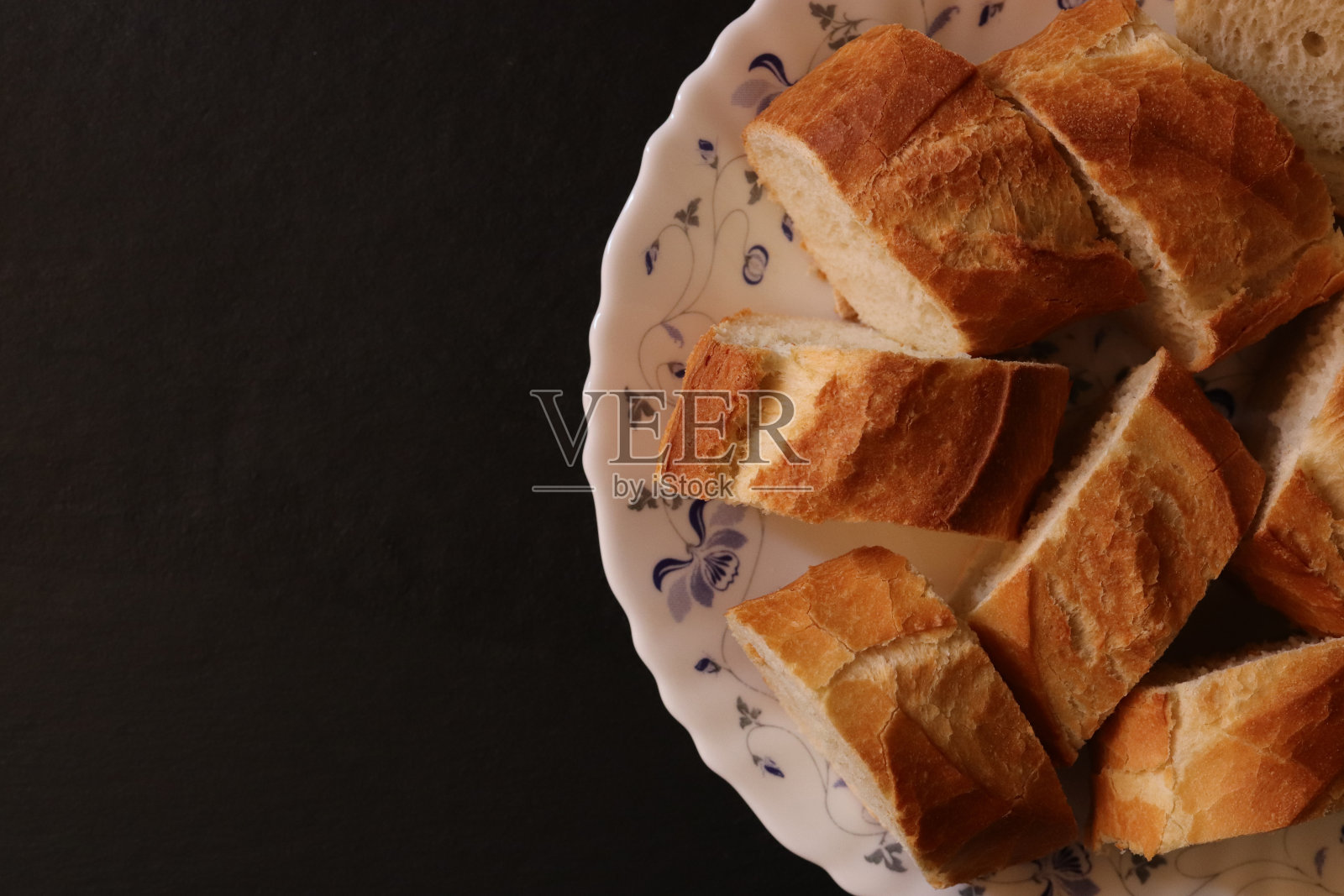 切好的法棍面包片放在盘子里。面包食物在黑色背景上。照片摄影图片
