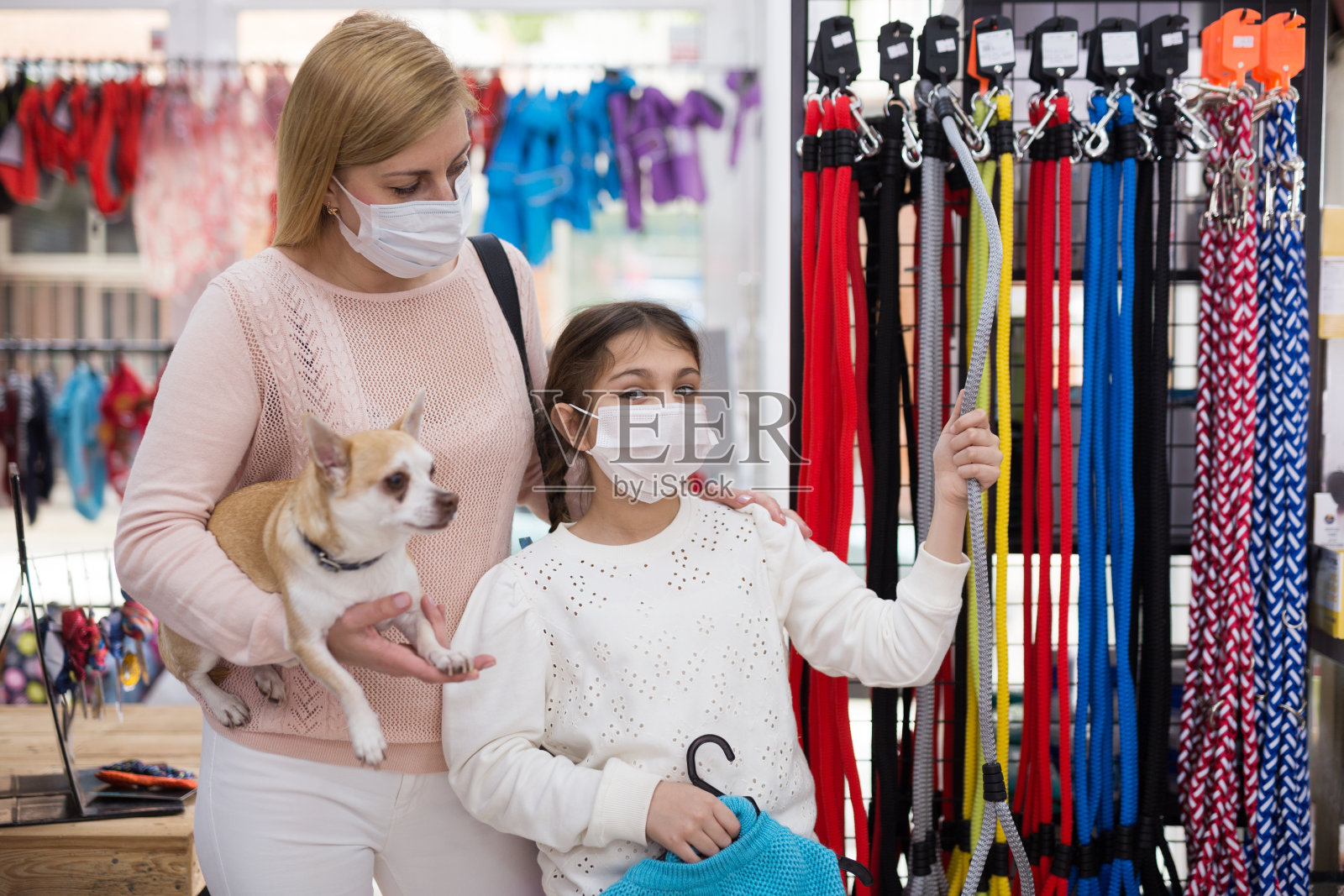 戴面具的女人在宠物店购物,她的女儿和狗照片摄影图片
