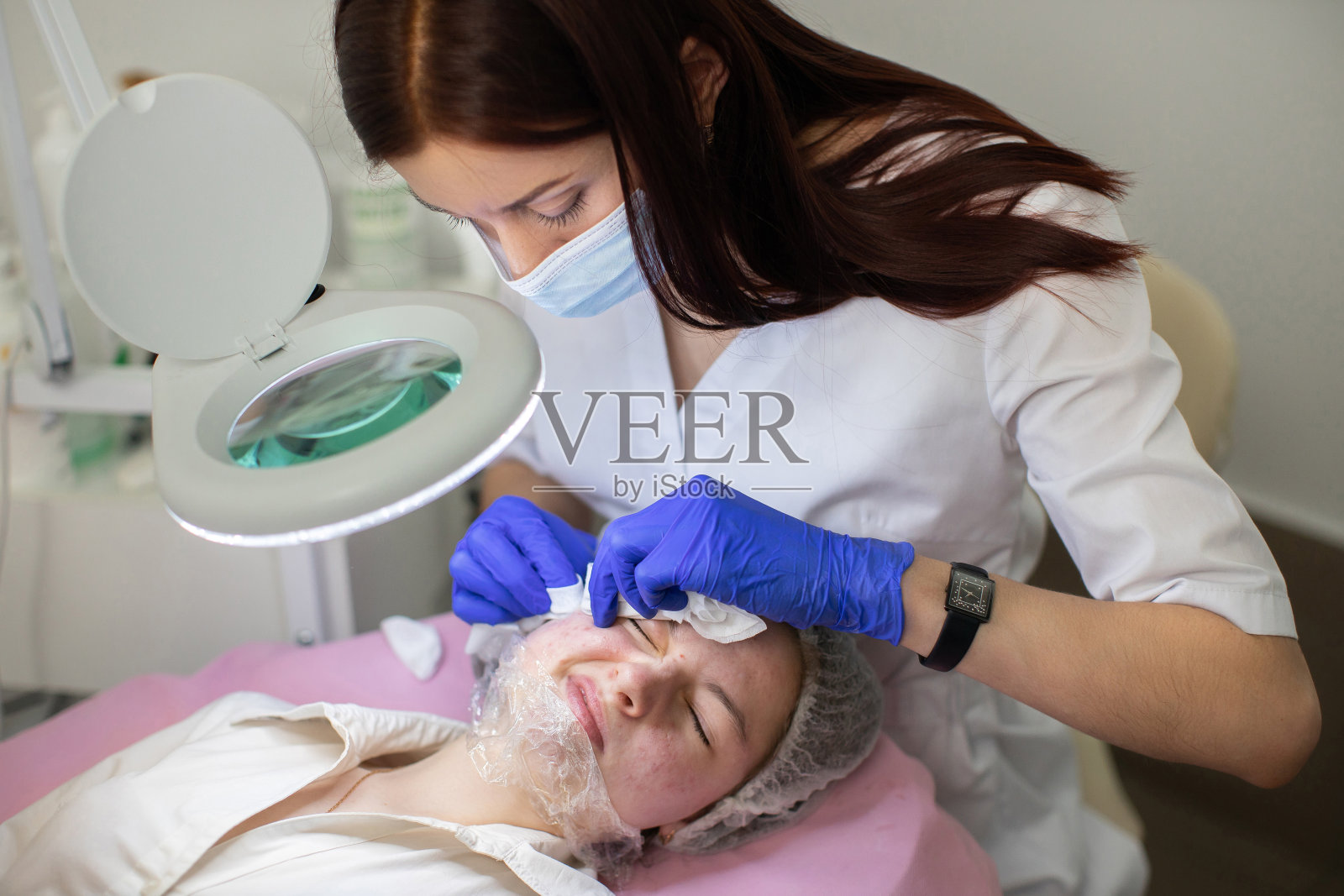 在美容师办公室机械清洁面部。女医生美容师正在处理和清洗脸上的痤疮年轻少女的脸使用擦拭垫。照片摄影图片