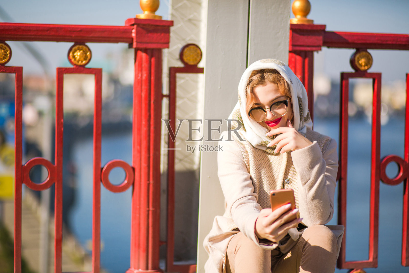 微笑的金发模特身穿米色外套,披着白色披肩,用她的智能手机打字照片摄影图片