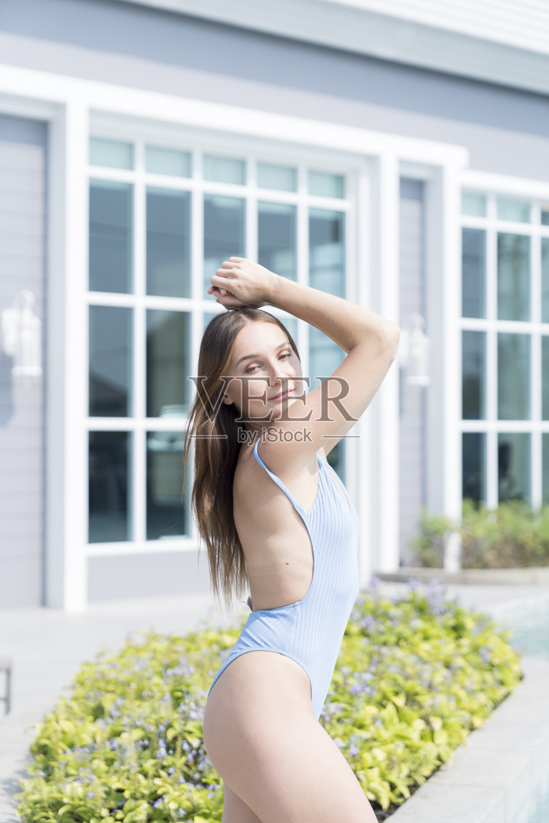 一个穿着游泳衣的年轻女子在泳池边的水里玩。一名年轻女子在热带度假胜地学习泳装游泳。照片摄影图片