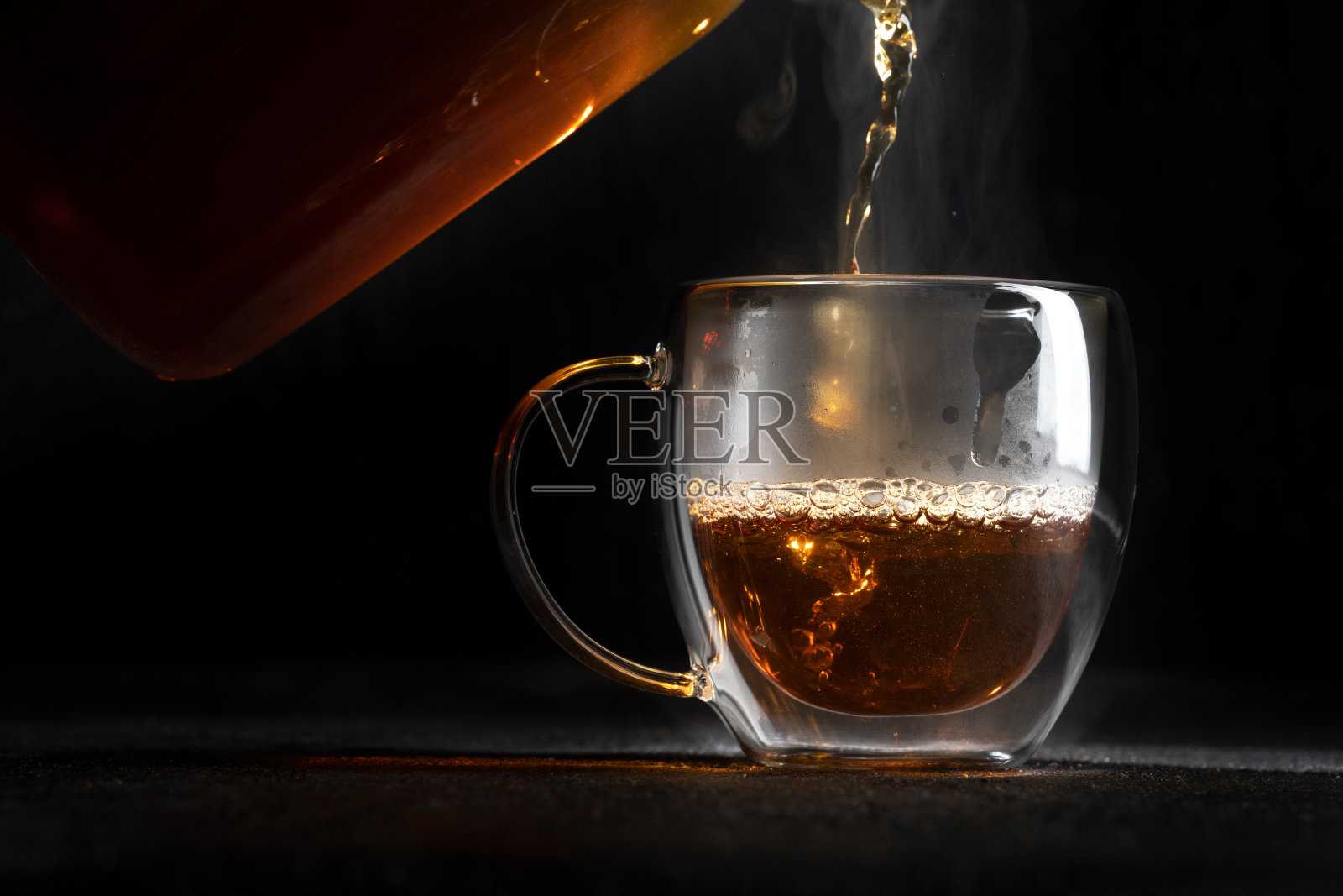 热茶倒进一个黑色背景的透明杯子里照片摄影图片