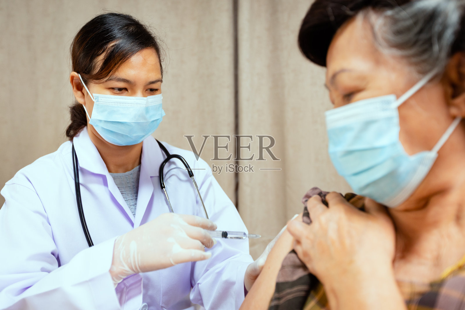 医生为老年妇女手臂注射疫苗。医生和成年患者佩戴防护口罩,以保护冠状病毒Covid-19大流行。照片摄影图片