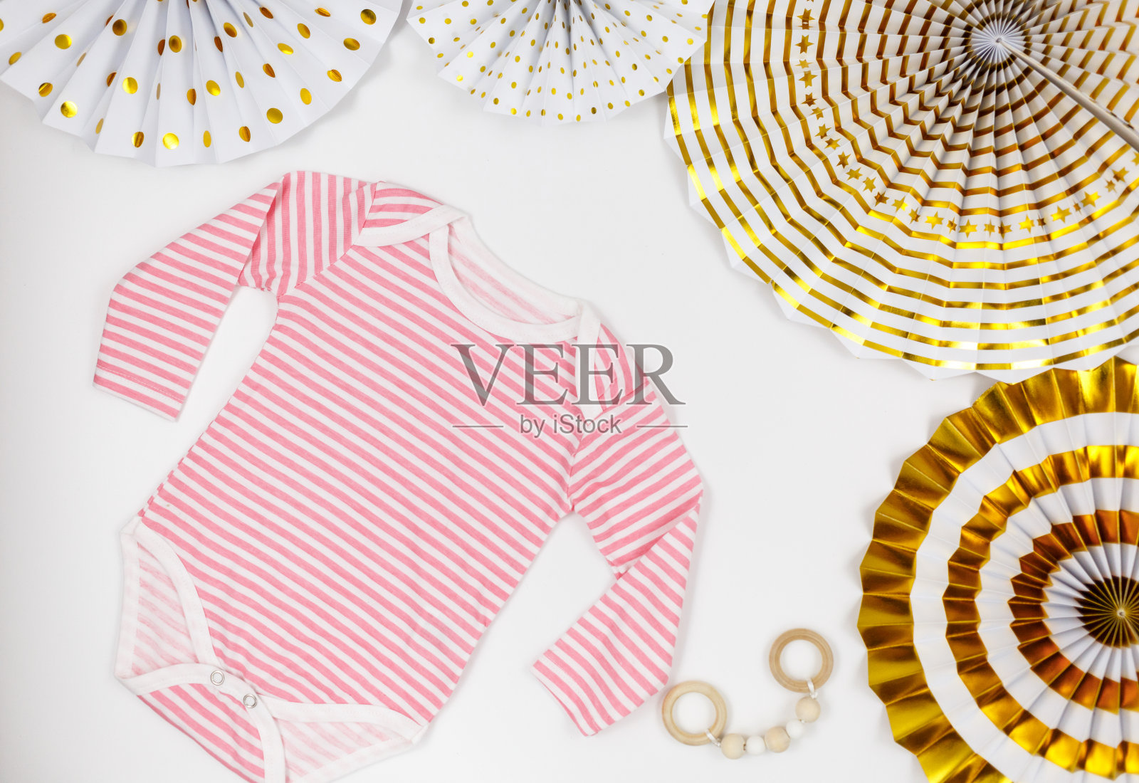 白色的桌子上放着粉色的紧身衣、纸扇和新生儿的配件。有机棉婴儿紧身衣模型与环保木制玩具。宝宝送礼会、节日、生日派对装饰照片摄影图片