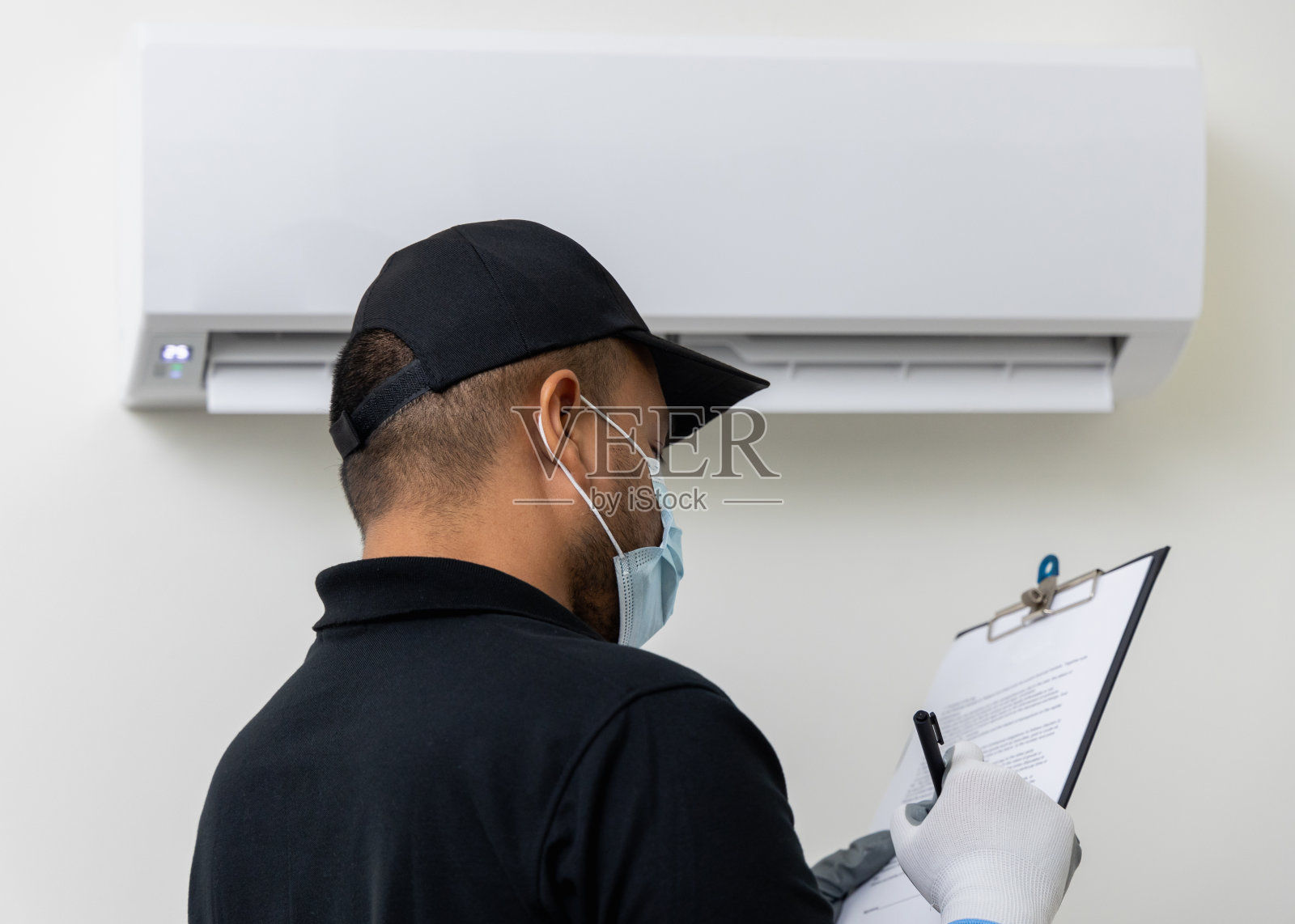 室内空调服务。亚洲技术员检查清单并修理空调。空调清洁人员清除堵塞的过滤网。他穿着制服,戴着橡胶和面具。照片摄影图片