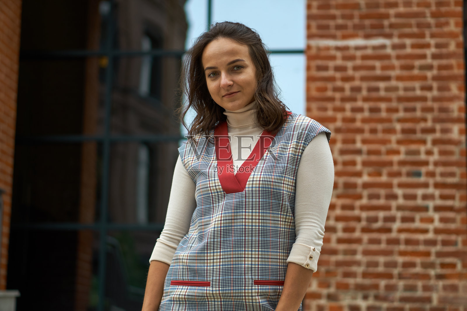 一个穿着牛仔布的女人走在砖墙之间。黑发的女子笑着说。红色衣领。照片摄影图片