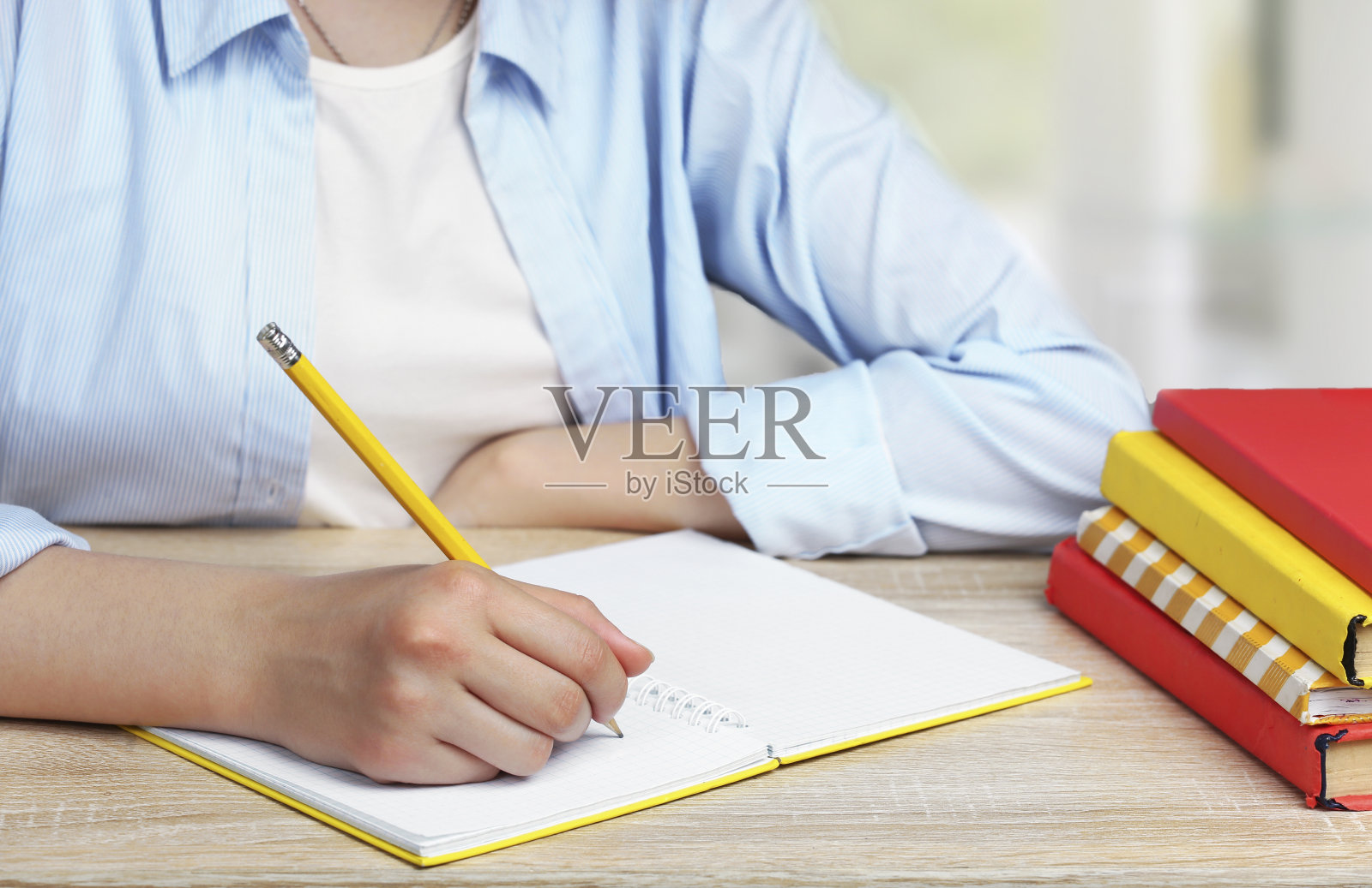 小女孩用铅笔在抄写本上写字。学生坐在课桌前,堆着书。学校作业。学习的过程。教育的概念。照片摄影图片