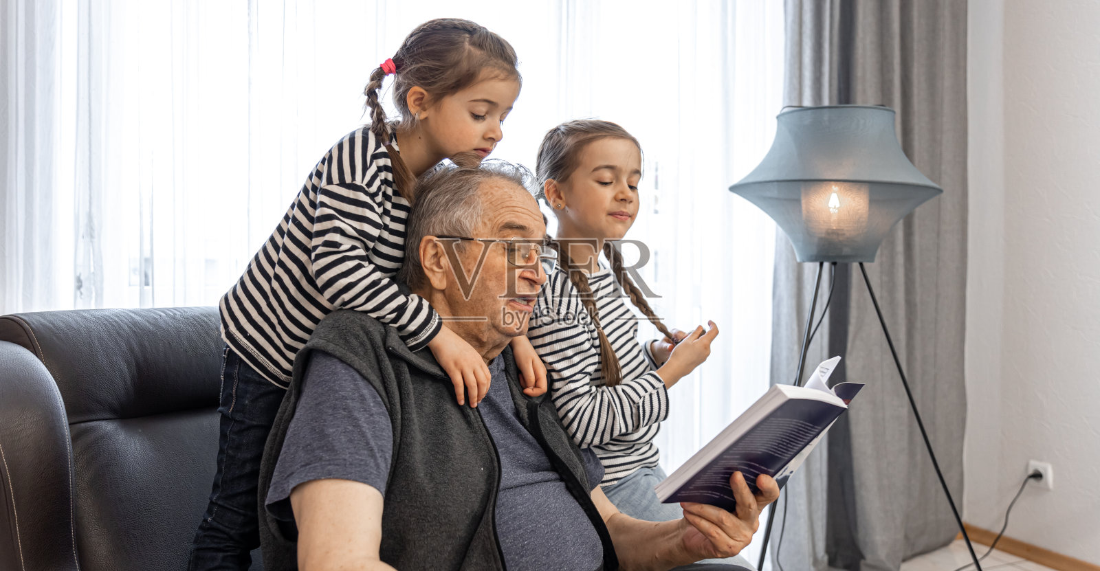 爷爷和他的孙女们一起读书。照片摄影图片