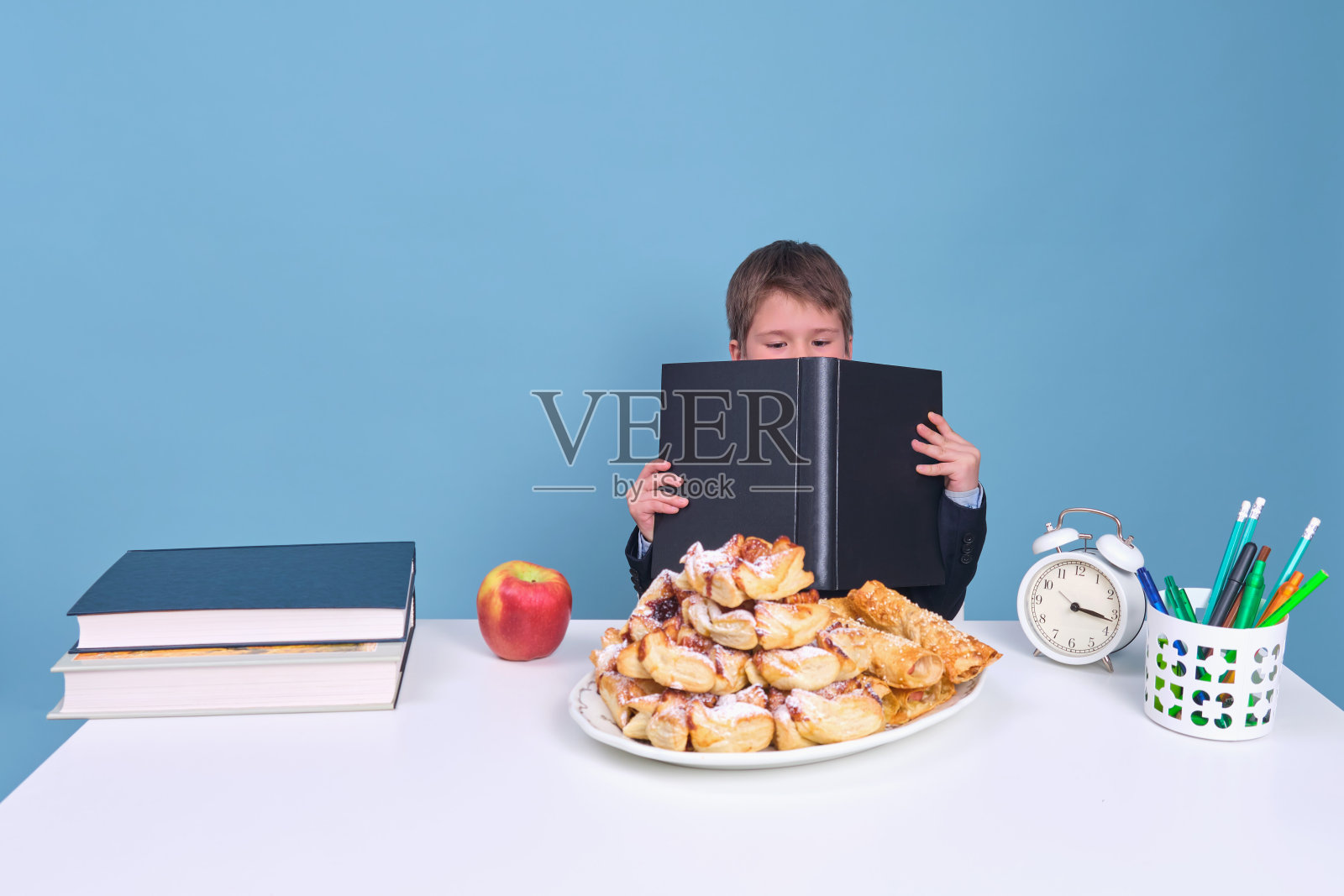 男生穿着校服,桌上放着书本和食物,蓝色背景的课本照片摄影图片