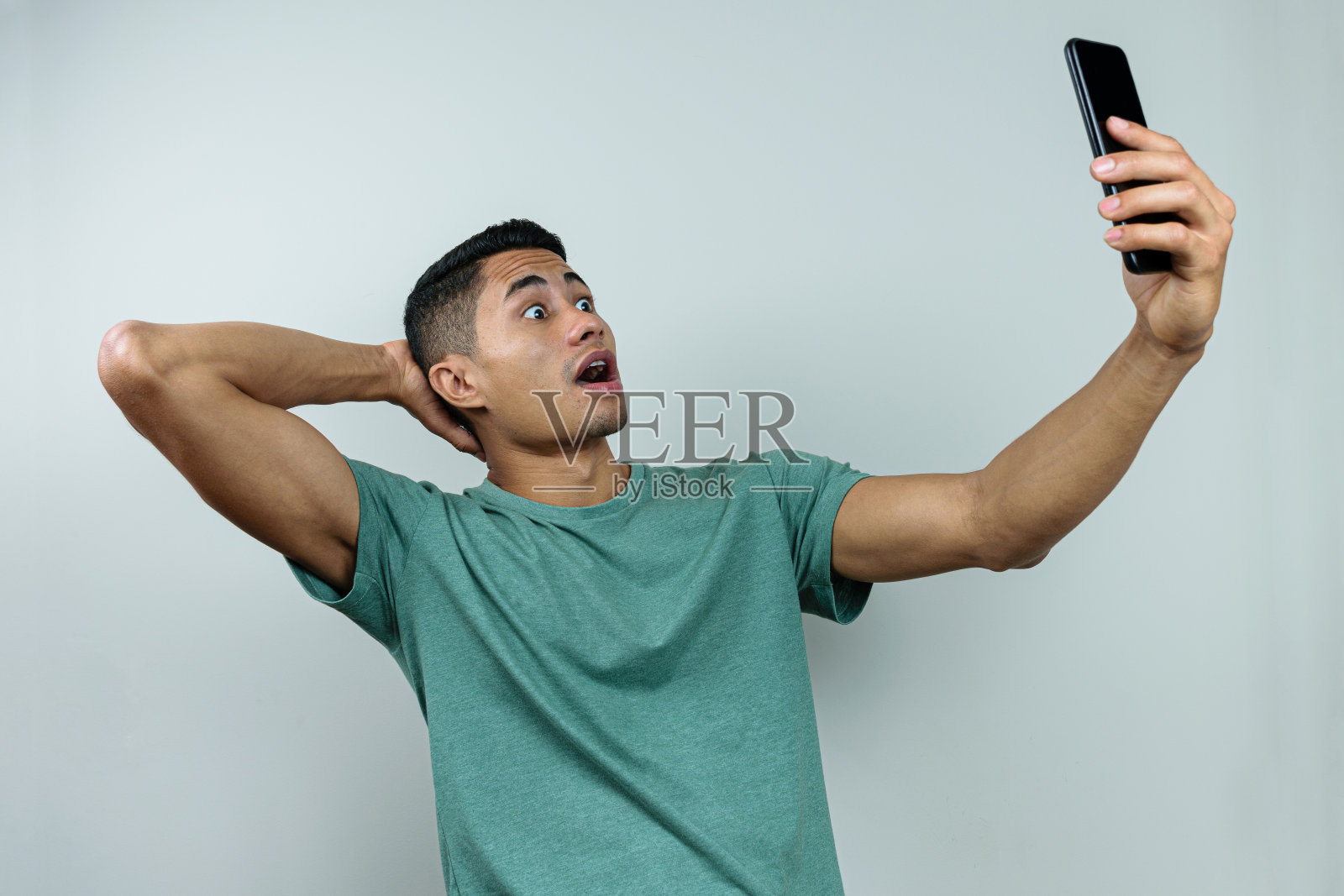 28岁的巴西年轻人,睁大眼睛盯着手机看,另一只手放在脖子后面(惊讶)。照片摄影图片