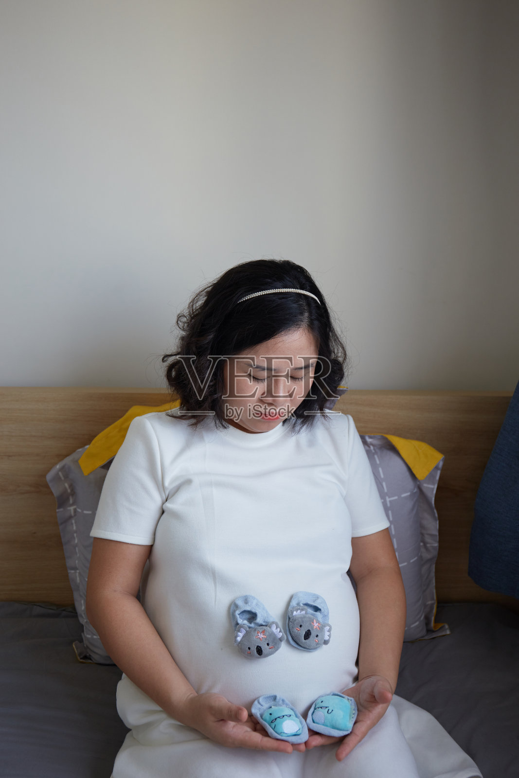 越南一名年轻孕妇躺在床上,肚子上放着一双婴儿鞋照片摄影图片