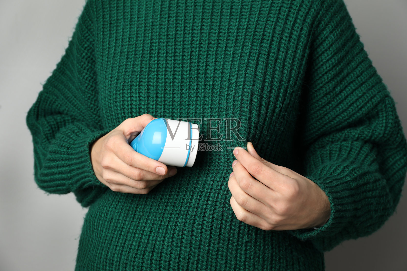 女人在羊毛衫使用织物剃须刀在浅灰色的背景,特写照片摄影图片