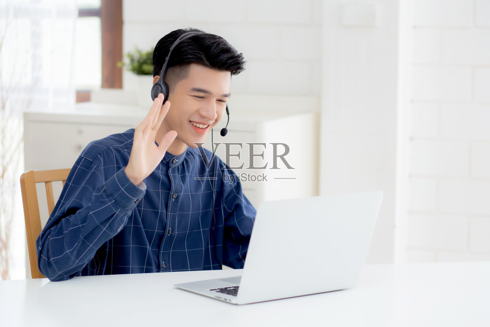 年轻的亚洲商人在家里用笔记本电脑工作时戴着耳机,商人戴着耳机进行视频会议、通信和教育,男性学习和学习为电子学习。照片摄影图片