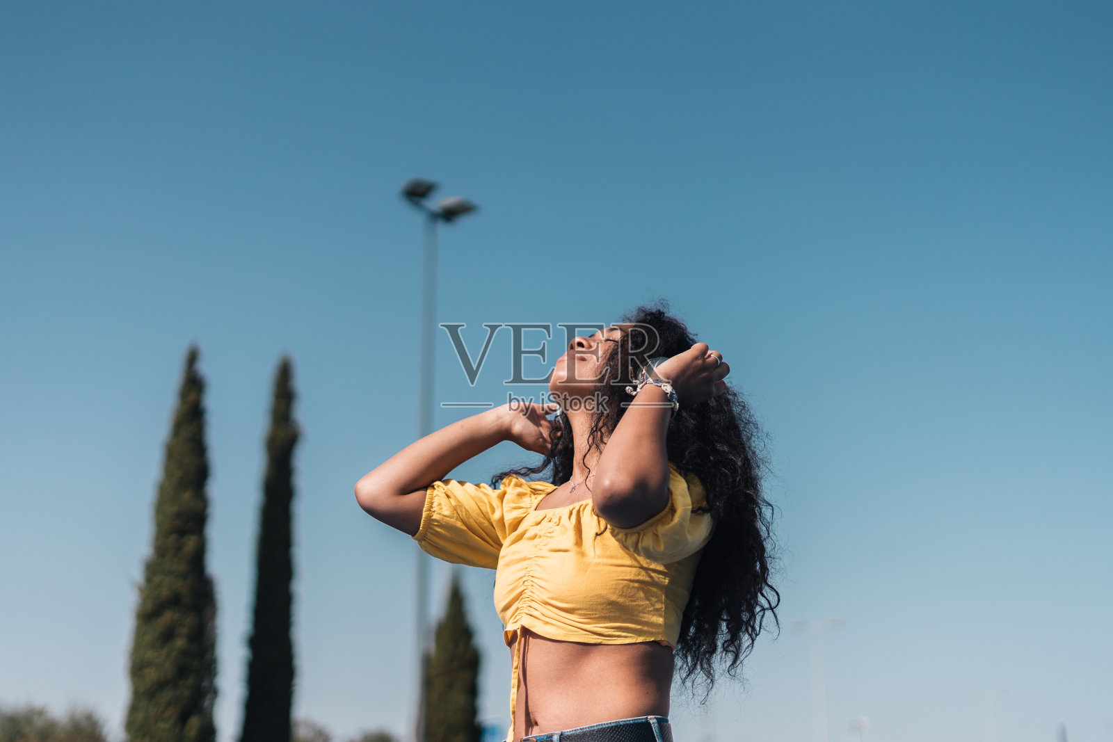 年轻的非洲裔美国妇女快乐地穿着黄色t恤,长长的卷发戴着耳机。照片摄影图片