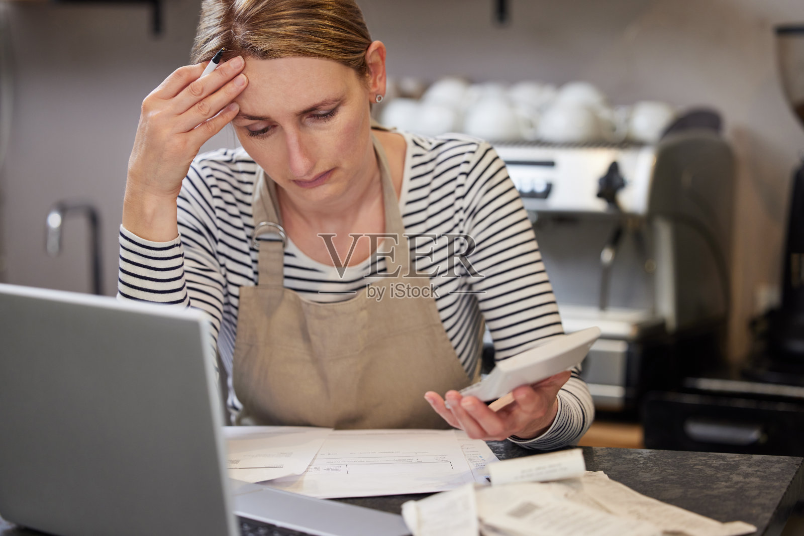 咖啡店的女老板在财务困难中使用笔记本电脑和计算器查看账单照片摄影图片