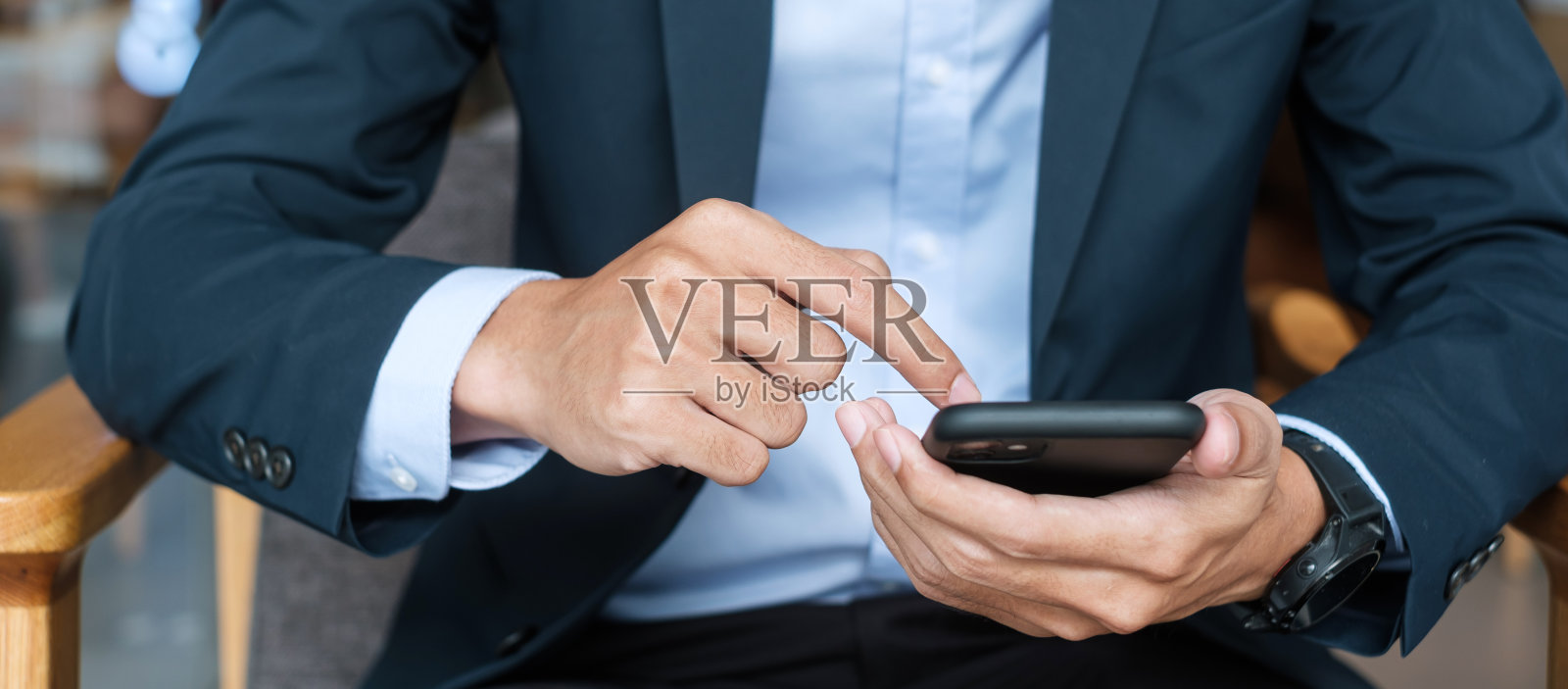 穿着西装拿着智能手机发短信的年轻商人,在办公室或咖啡馆里输入触屏手机的男人。商业,生活方式,技术和社交媒体网络概念照片摄影图片