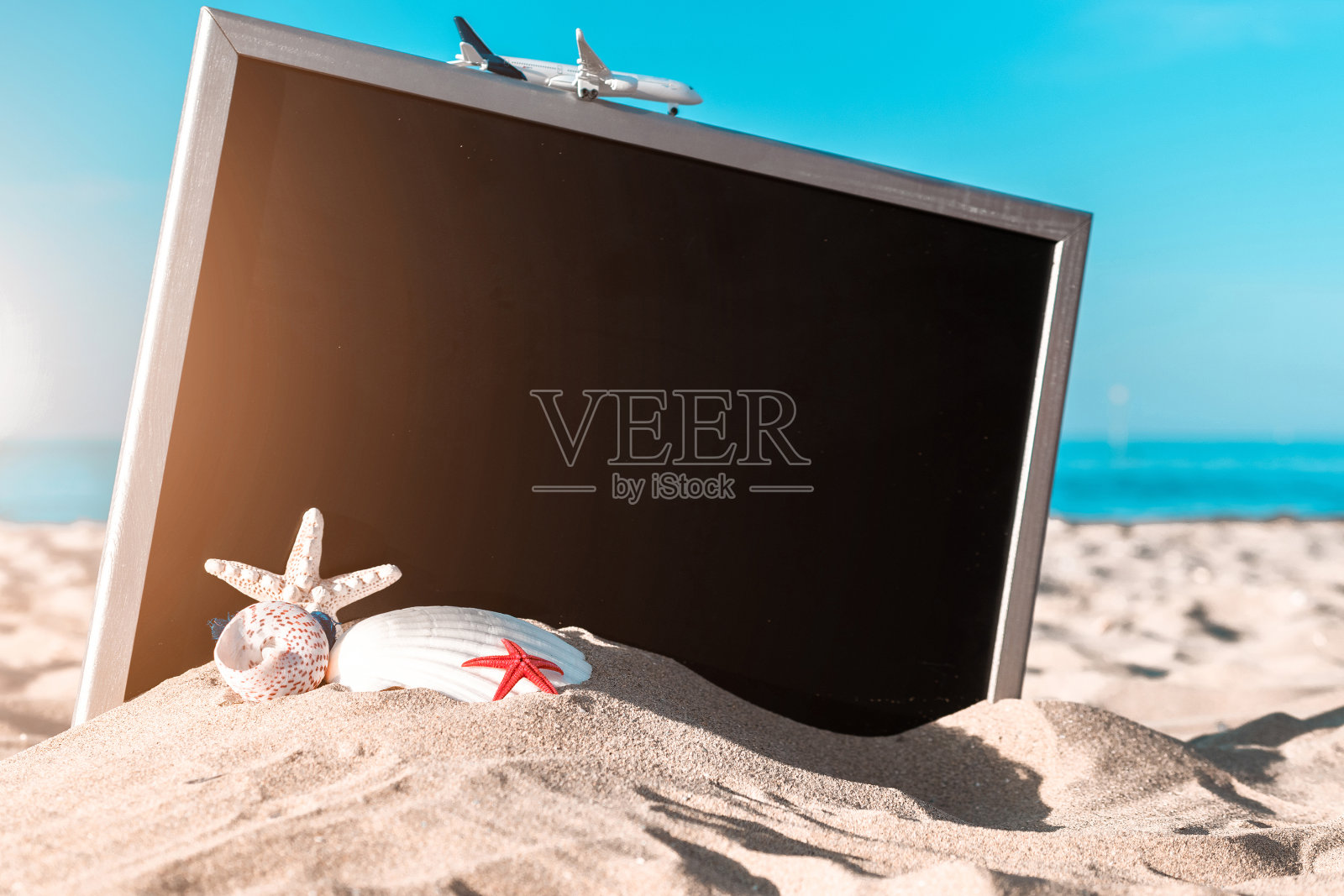 海的背景。在阳光明媚的日子里,海滩上的黑色书桌旁有地球仪、贝壳、飞机和海星。带有复印空间的异国情调热带海滩。照片摄影图片