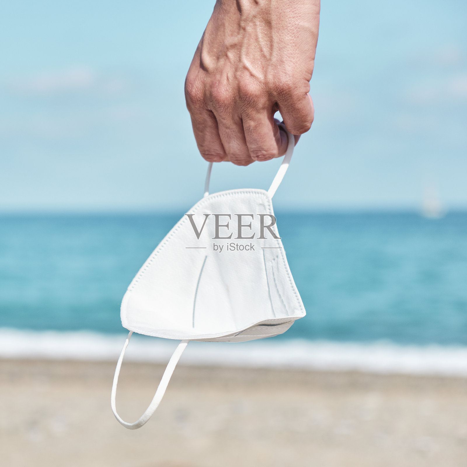 在海滩上,一个手拿FFP2面罩的男人照片摄影图片