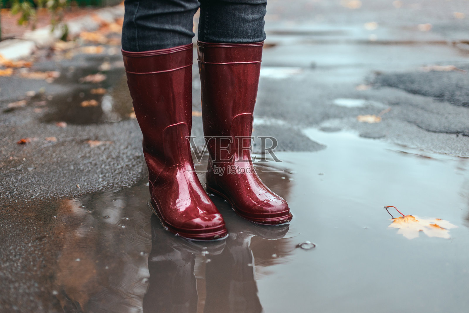 秋日的雨天,穿着红色橡胶靴子的女性双脚站在泥泞的水坑里照片摄影图片
