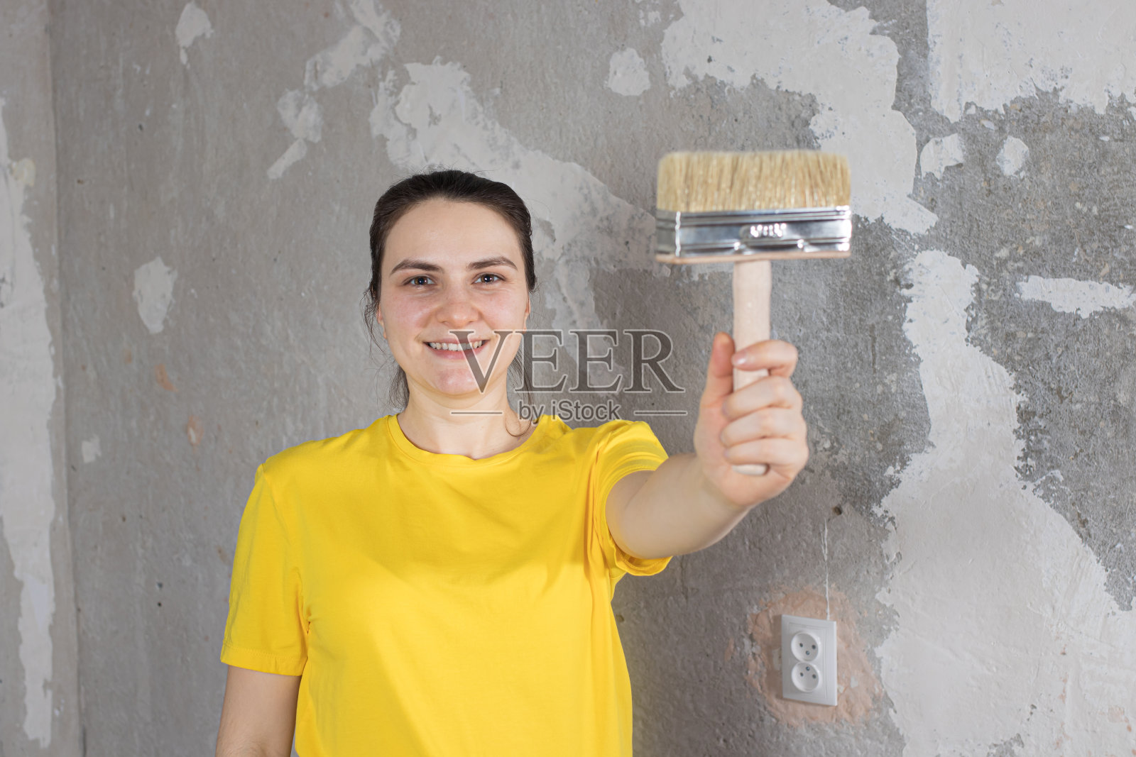 一个穿着黄色鲜艳t恤的女修理工拿着一把刷子微笑着。为文本复制空间。照片摄影图片