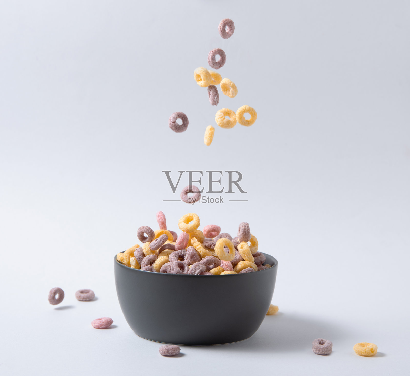 在灰色的背景下,黑色的碗里飞着五颜六色的甜玉米片。前视图和复制空间照片摄影图片