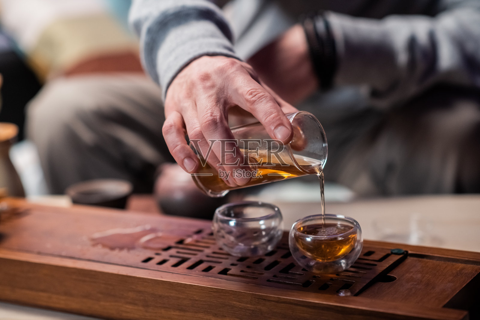 一个男人的手拿着一个玻璃壶的茶在特写中倒热饮到一个杯子。中国真正茶道的秘密照片摄影图片