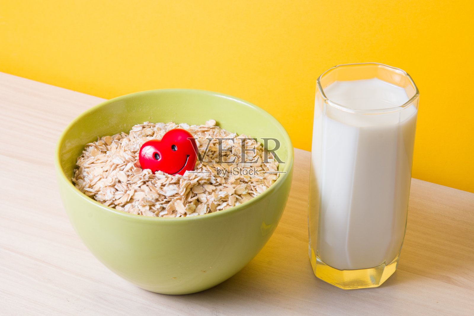 燕麦片在一个绿色的碗和一个红色的快乐心和一杯牛奶在木桌上,保健,饮食和适当的食物,麸质和乳糖耐量,黄色的背景照片摄影图片