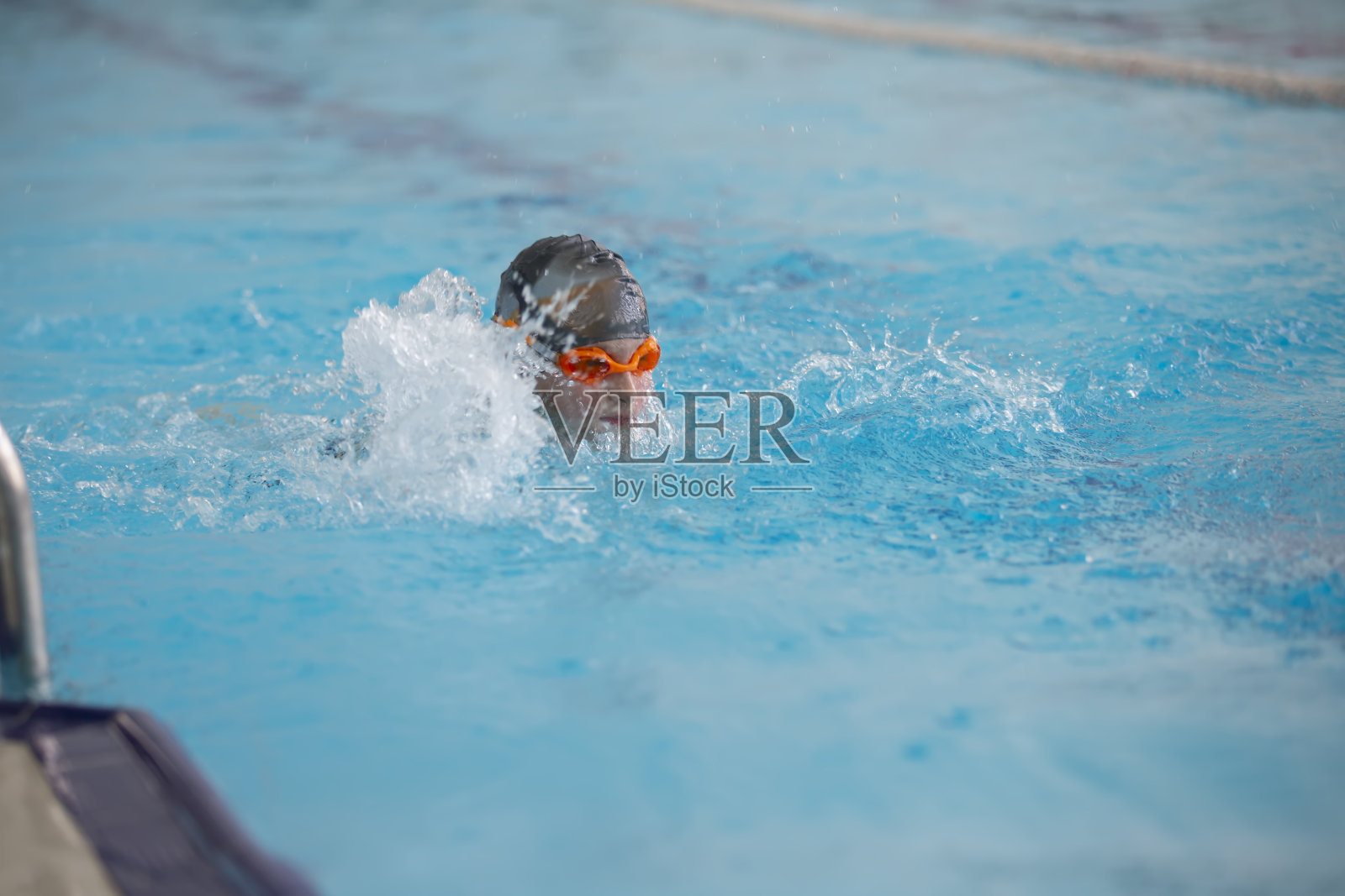 一个戴着游泳帽和眼镜的男孩正在运动游泳池里游泳。照片摄影图片