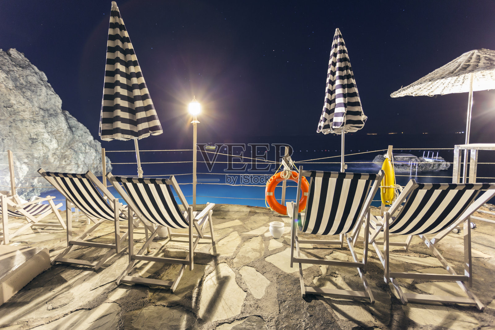 晚上晒太阳的人站在岩石海滩上。照片摄影图片