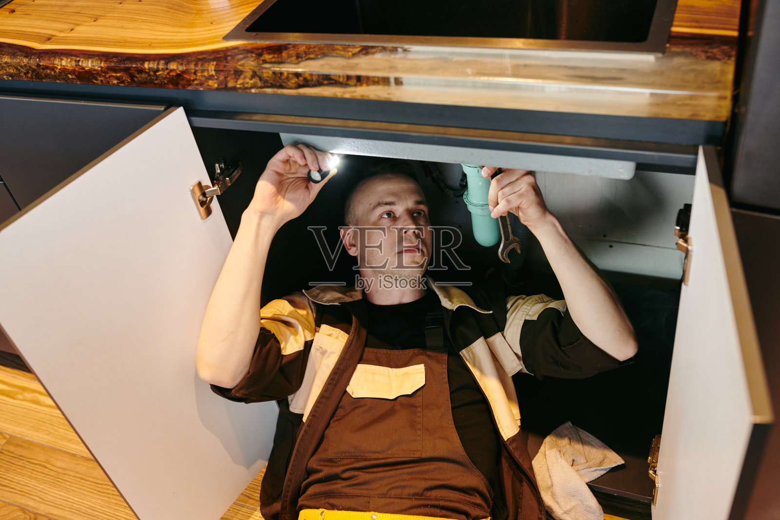 穿着制服的年轻水管工正在修理厨房水槽照片摄影图片