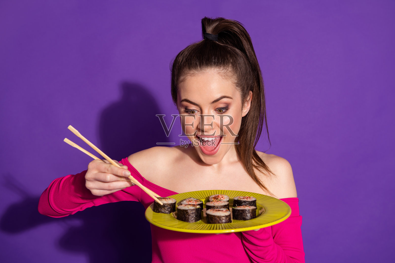 特写吸引人的快乐饥饿的女孩吃新鲜美味的卷孤立在明亮的紫罗兰色背景照片摄影图片