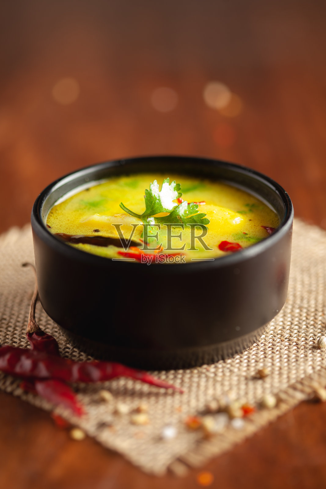 健康咖喱酸奶和土豆(Dahi Aloo或Aaloo)的特写,这是印度的一道经典菜肴。盛在黑碗里,四周放着香料。木制背景和黄麻垫子。照片摄影图片