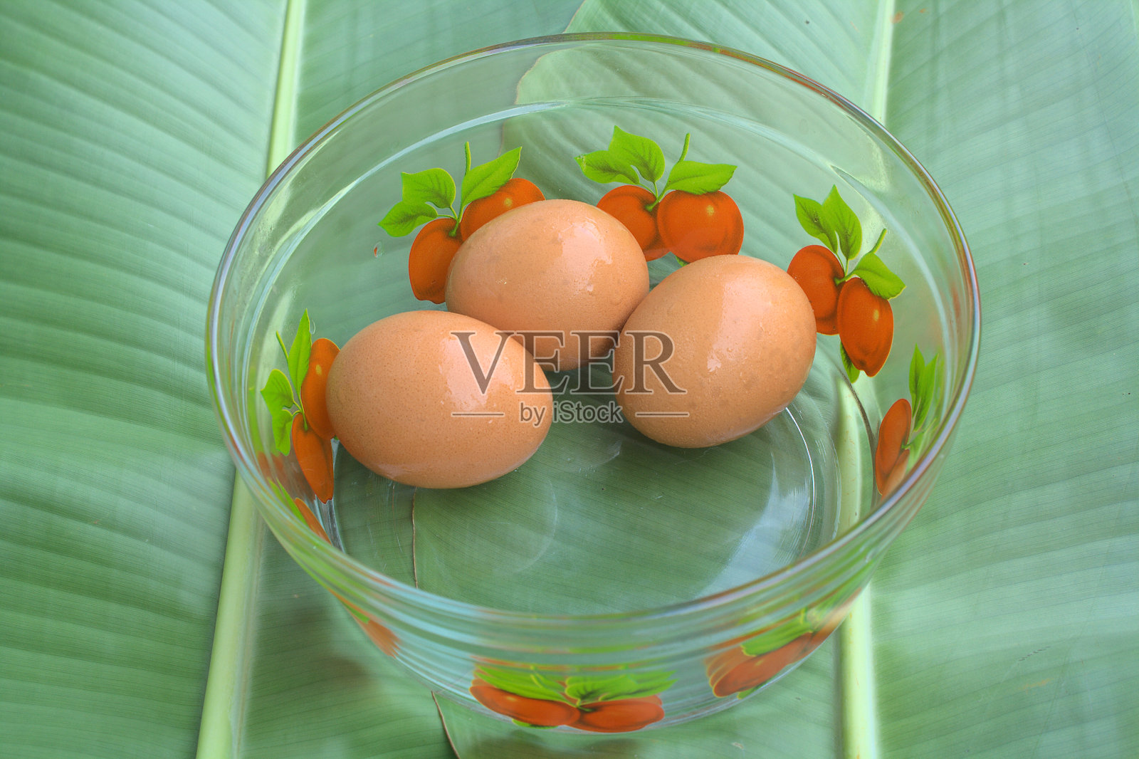 三个鸡蛋放在一片叶子上的玻璃杯里。照片摄影图片