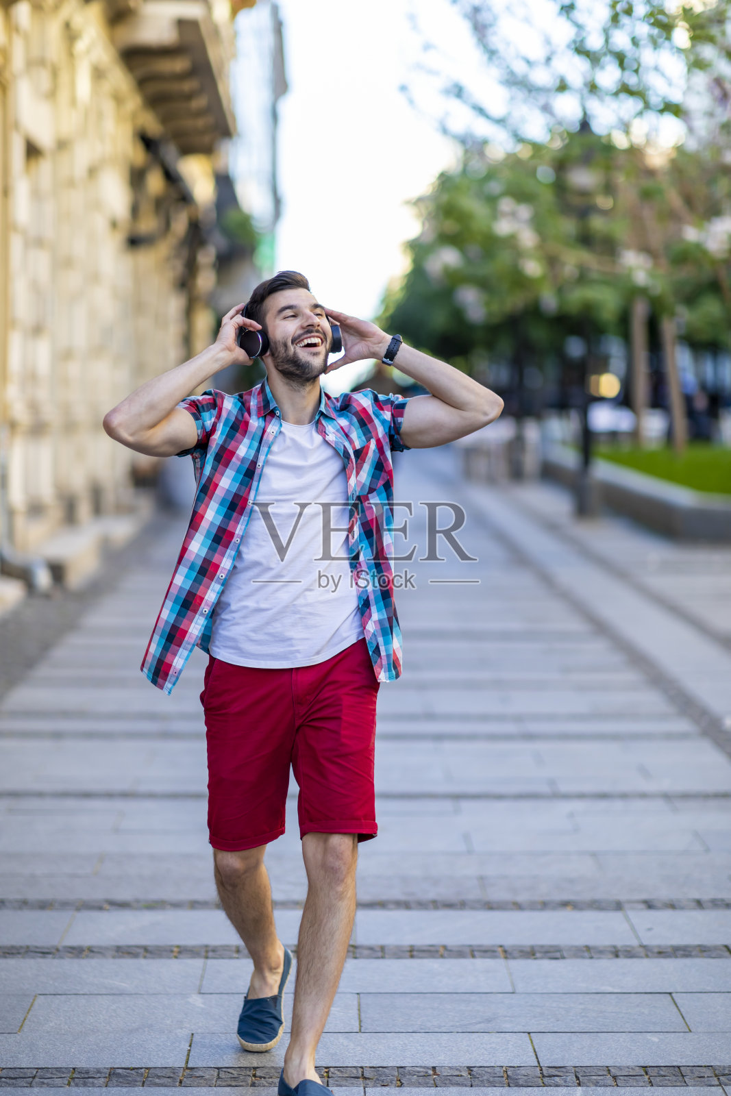 微笑的年轻迷人的男子听音乐在街上照片摄影图片