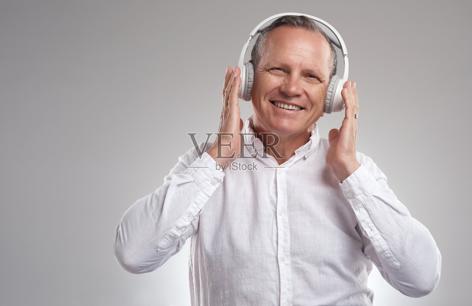 一个英俊成熟的商人站在一个灰色的背景下,在工作室里通过耳机听音乐的照片照片摄影图片