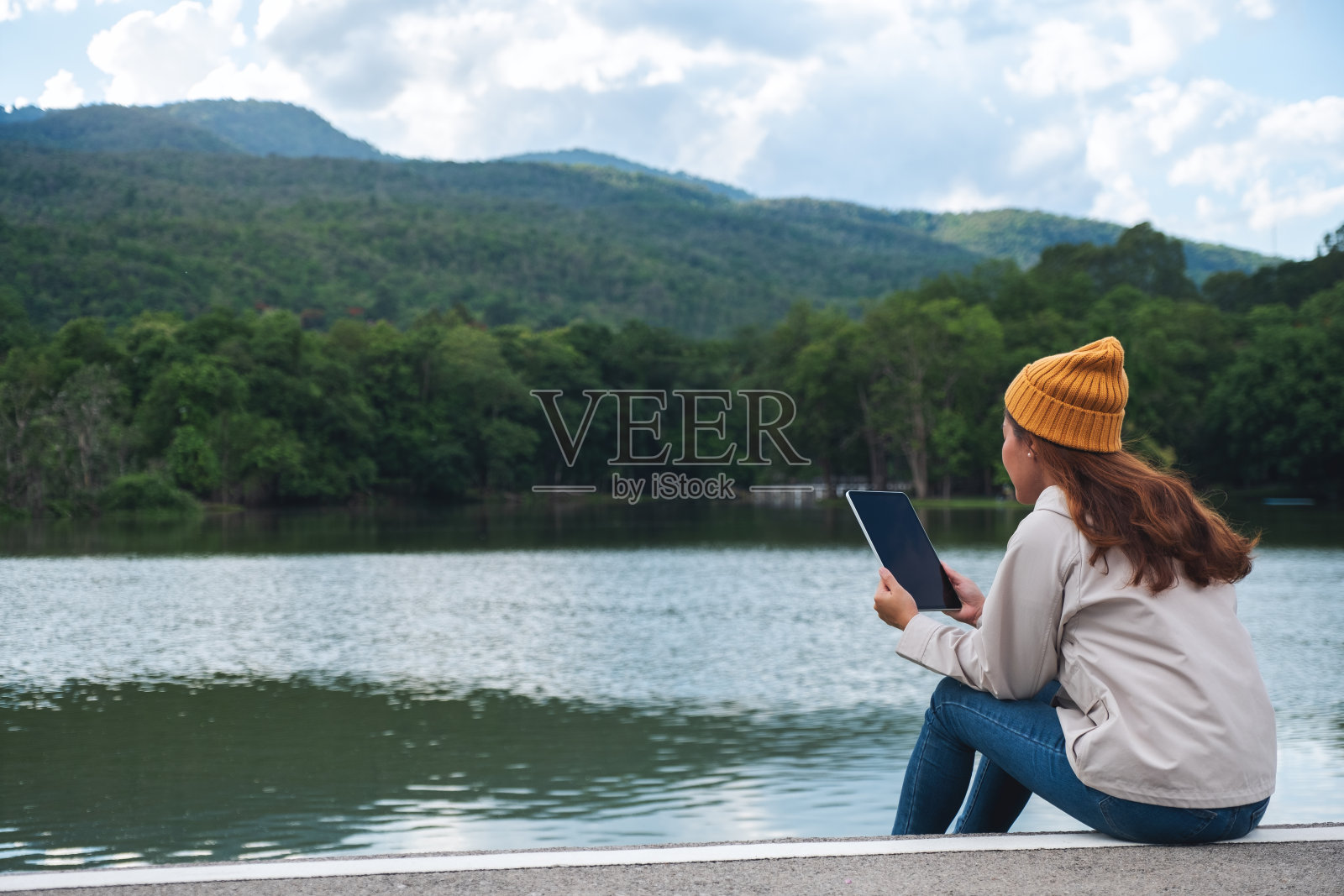 一个年轻的女人拿着并使用数字平板电脑在山和湖旅行照片摄影图片