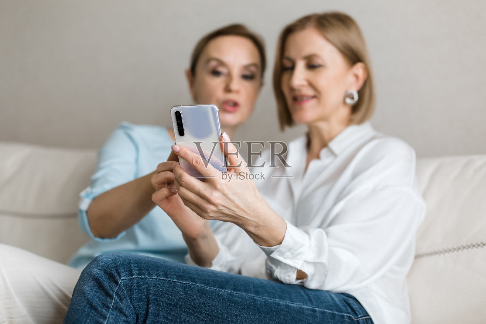 两个女人坐在沙发上一边看手机一边聊天。照片摄影图片