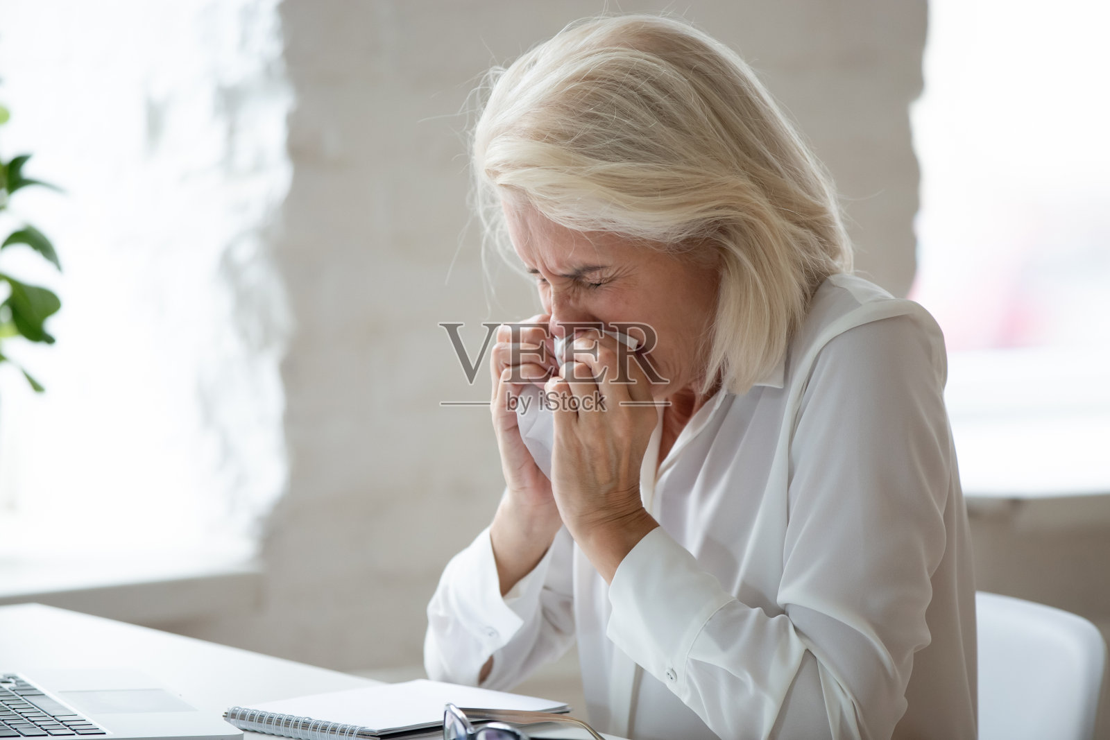 不快乐的60岁女商人近距离打喷嚏。照片摄影图片