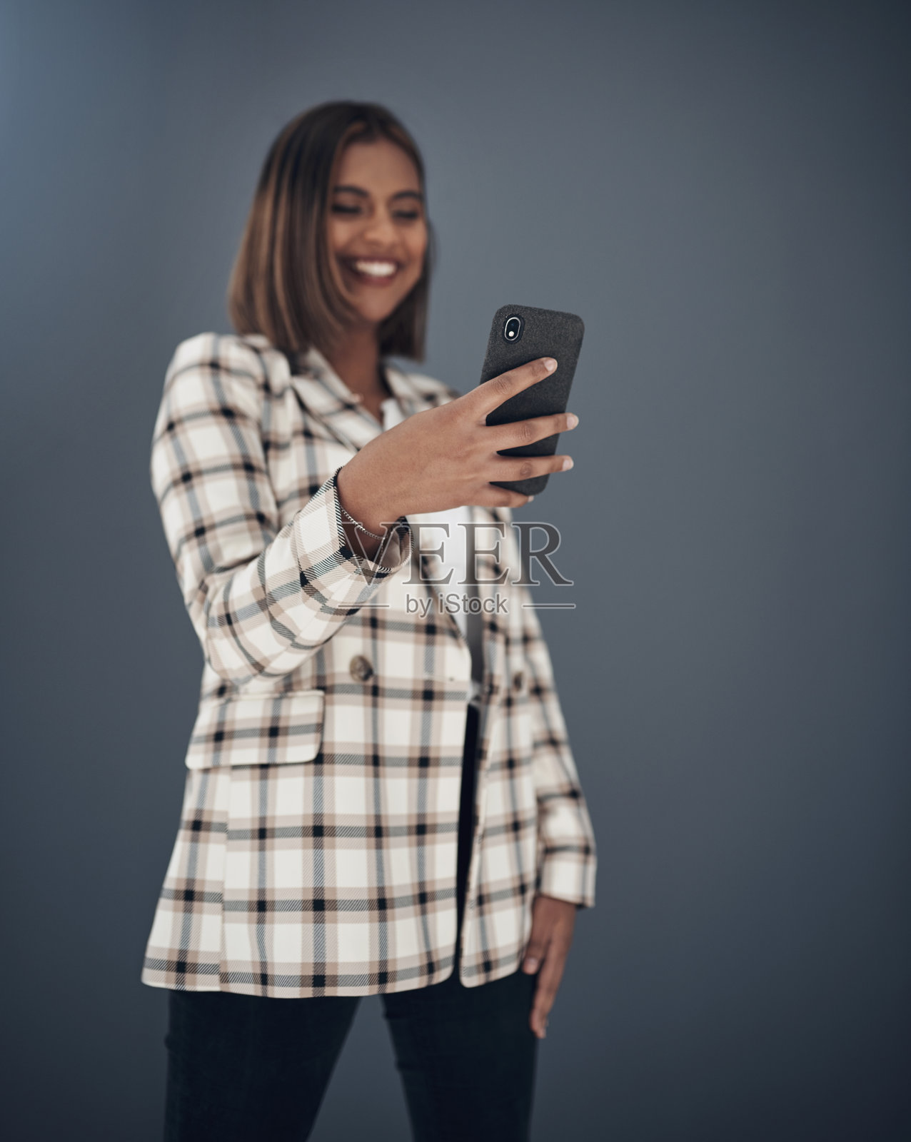 照片中,一位迷人的年轻女商人站在灰色的背景下,在办公室里使用手机照片摄影图片