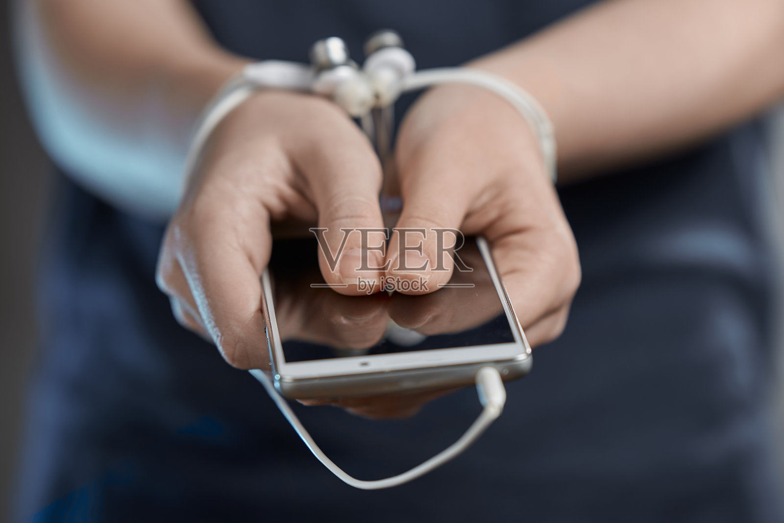 一个拿着智能手机的小女孩的手。沉迷于互联网和社交网络。双手用铁丝绑着。照片摄影图片