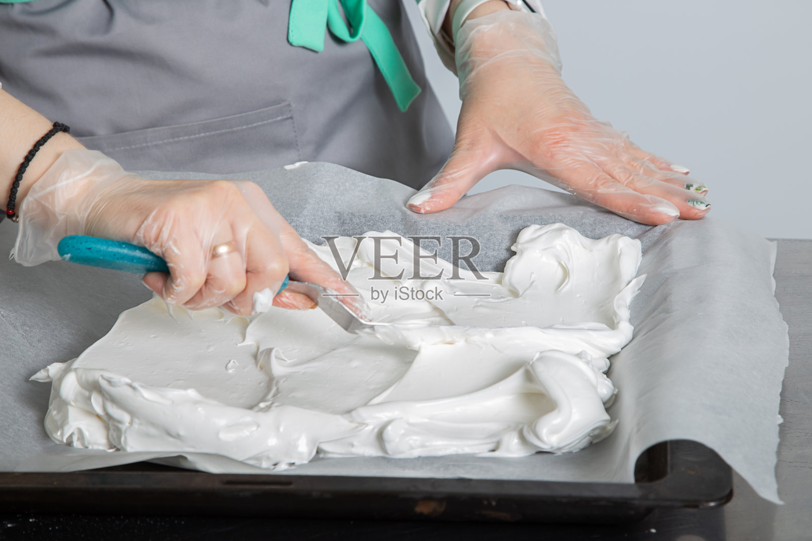 女厨师用手把混合的蛋白质铺在烤羊皮纸上。巴芙洛娃蛋糕的烹饪过程。照片摄影图片