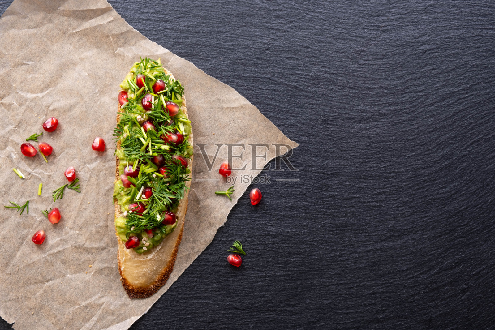 在背景的右侧,羊皮纸上,有一个由鳄梨、石榴和莳萝种子制成的canapé(特写)照片摄影图片