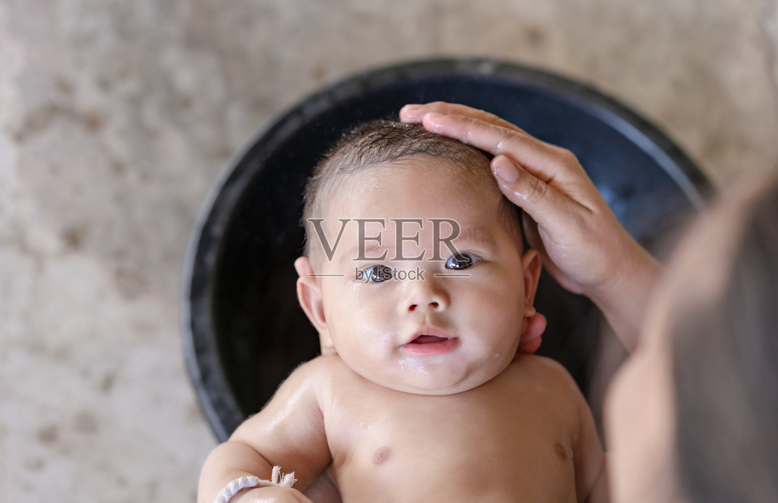 快乐微笑的新生儿正在洗澡,看着相机美丽的棕色眼睛。妈妈抱着小孩子在家里用可爱的笑容给小男孩洗头照片摄影图片