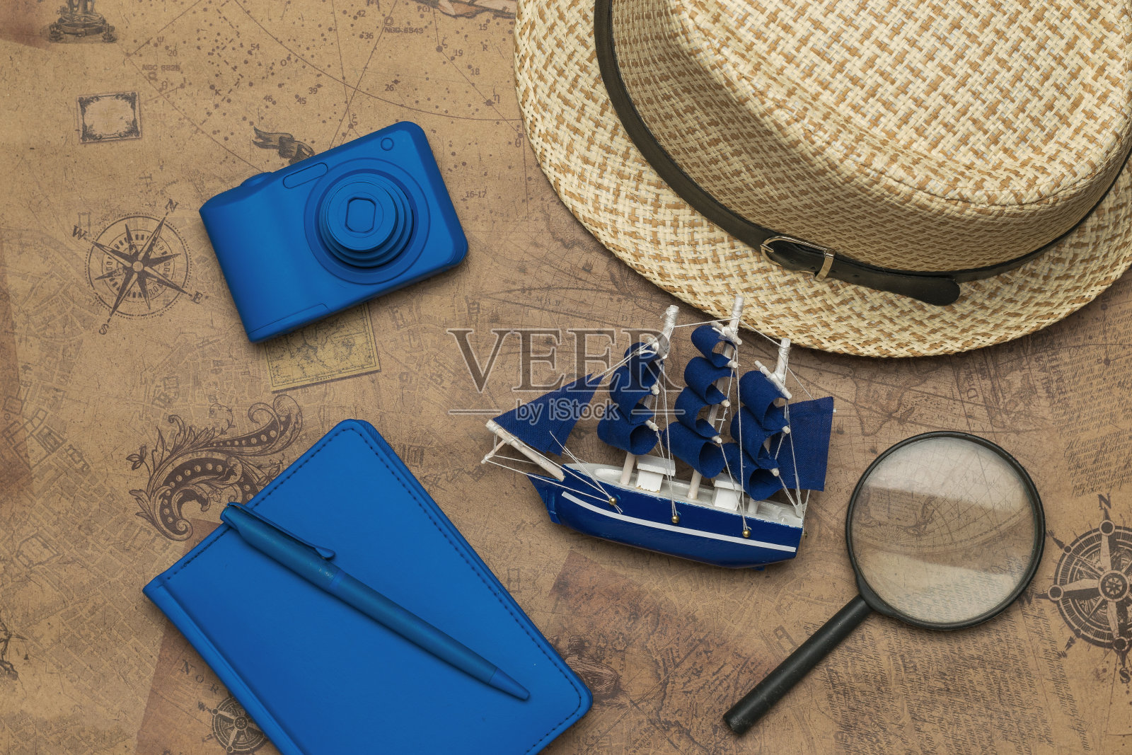 一顶帽子,一艘模型船,一架照相机和一个旧地图背景上的笔记本。照片摄影图片