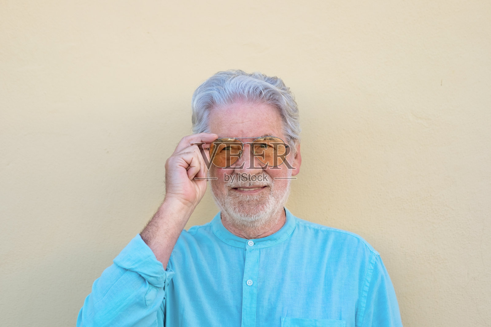 黄色背景上的白头发大胡子老人触摸着太阳镜照片摄影图片