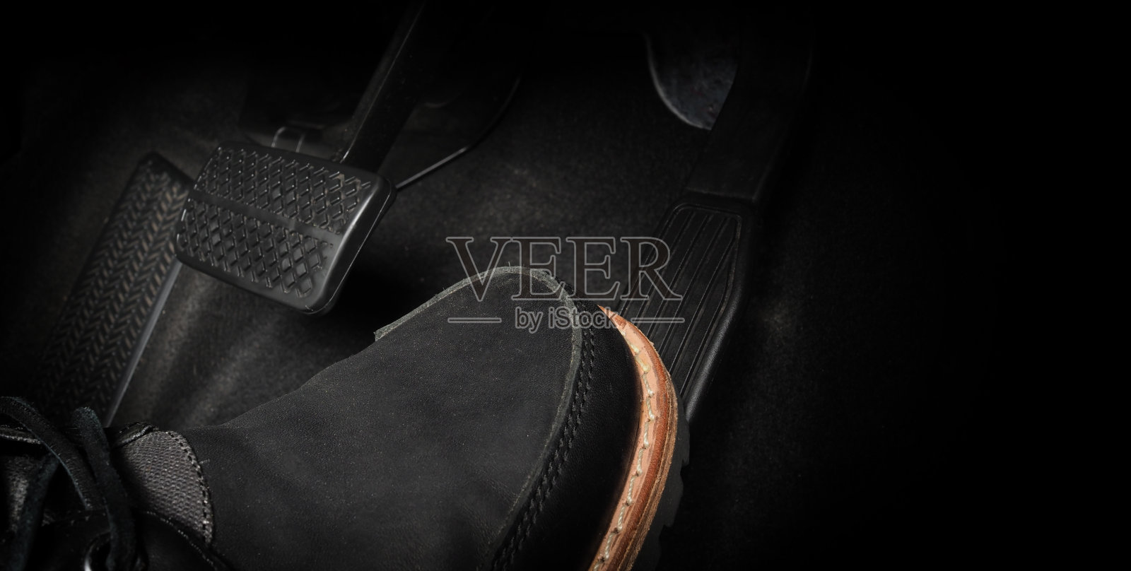 在开车时踩汽车的脚踏板。汽车的油门和刹车踏板。司机驾驶汽车通过推动加速器和刹车踏板的汽车。车辆内部。控制踏板。关闭了。照片摄影图片