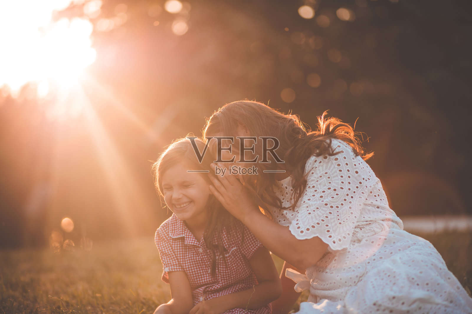母亲和女儿坐在草地上聊天。照片摄影图片